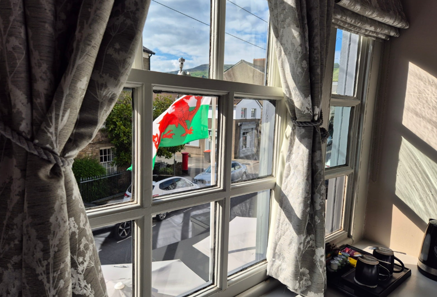 View through a guest room sash window onto Crickhowell High Street and the hills beyond, Welsh flag flying