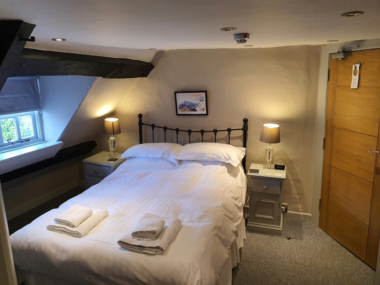Standard double room with brass bedstead, oak beams and a small window in the eaves
