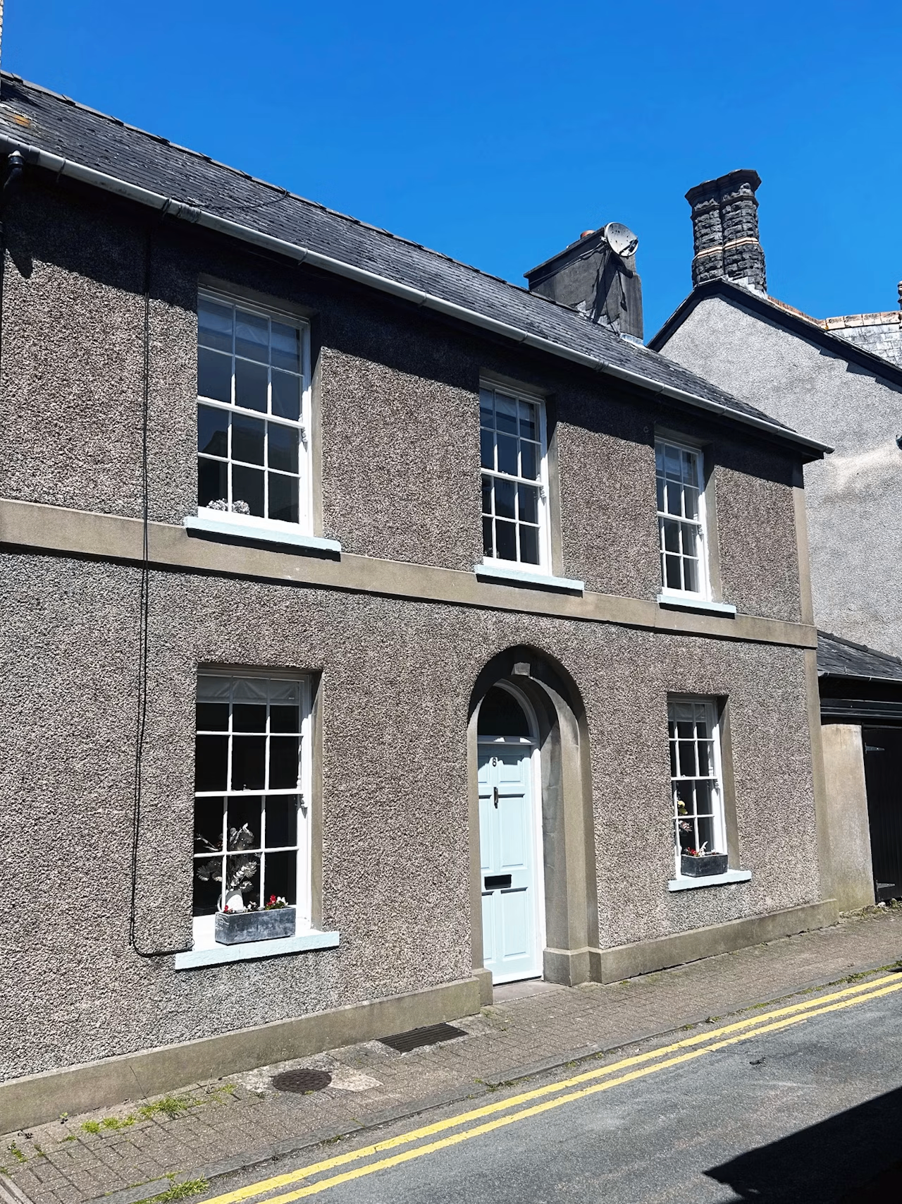 Two-storey stone town cottage with sash windows and arched white door on a Crickhowell side street